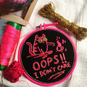 embroidered hoop art of cat tossing cup off the table and oops i dont care written