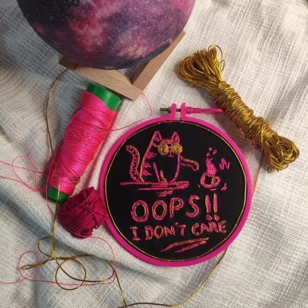 embroidered hoop art of cat tossing cup off the table and oops i dont care written